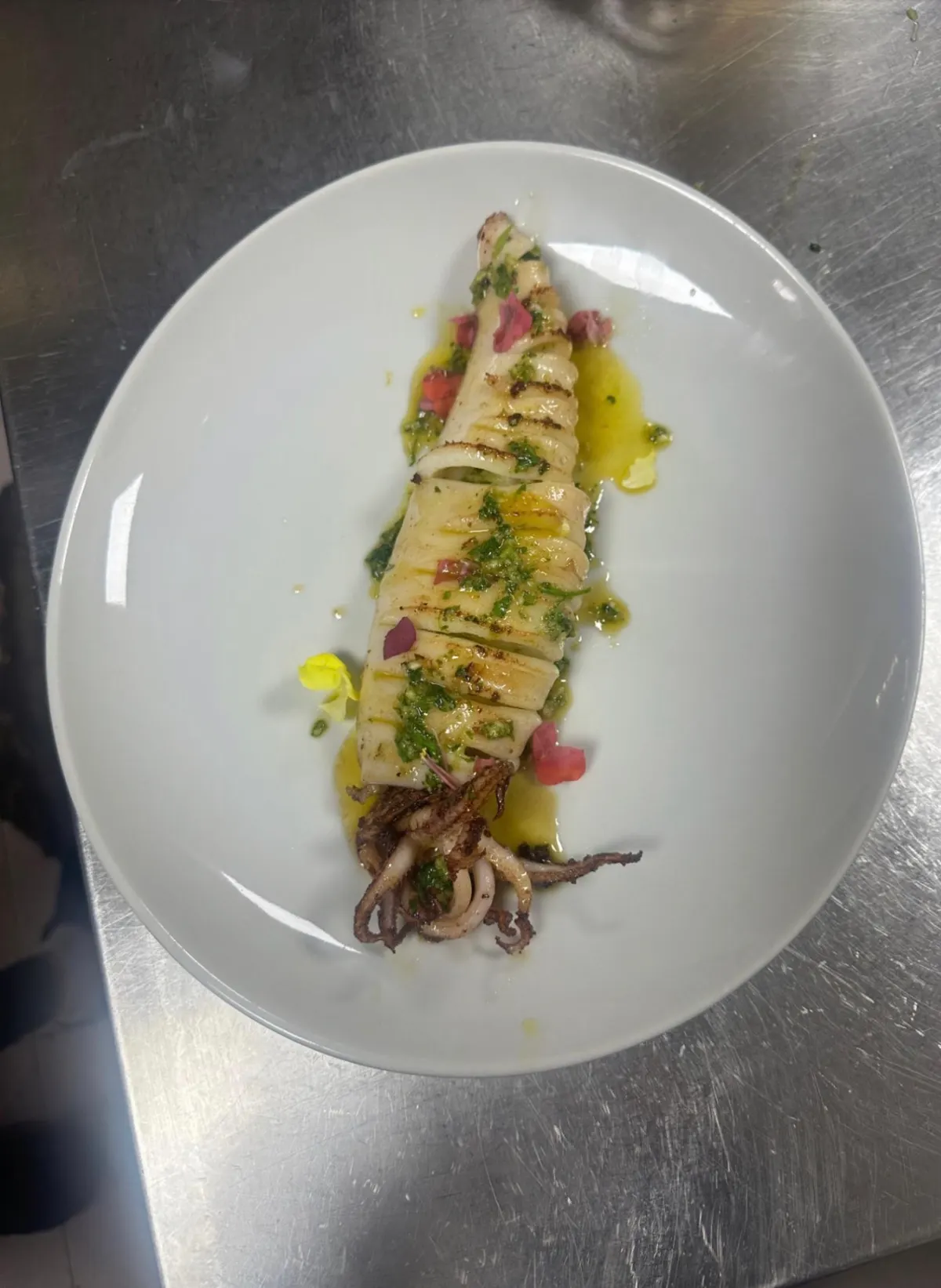 Pieza de sepia a la plancha con aceite de hierbas y tomate picado en un plato blanco ovalado